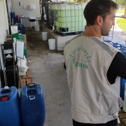 Duas pessoas realizam análises químicas. No local, diversos galões com produtos
