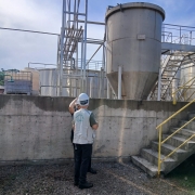 Duas pessoas utilizando capacetes de proteção conversam diante de complexo industrial
