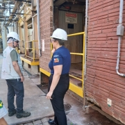 Duas pessoas utilizando capacetes de proteção observam construções de complexo industrial