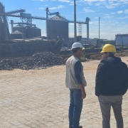 Quatro pessoas, utilizando capacetes de proteção, a céu aberto, em vistoria da Fepam. Ao fundo, um complexo industrial